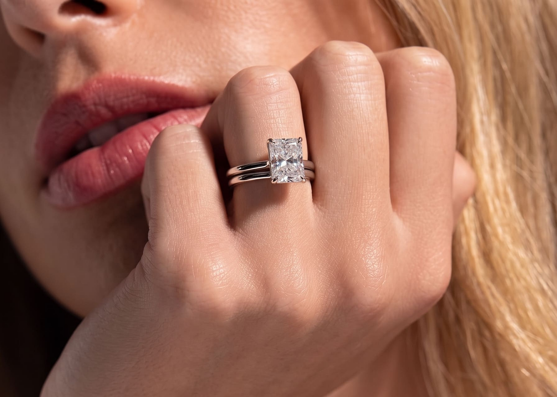 A close-up lifestyle shot of a woman's hand wearing a silver engagement ring with a large square princess-cut diamond and a matching silver band.